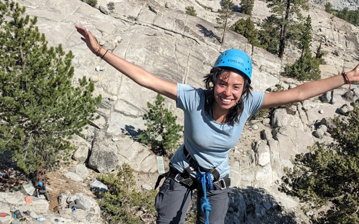 a student wearing rock climbing gear stretches out their hands in celebration